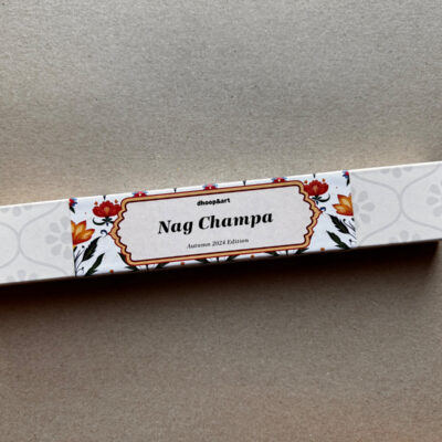 Räucherstäbchen-Verpackung 'Nag Champa' von dhoop&art Dresden, Autumn 2024 Edition. Die längliche weiße Box zeigt ein elegantes Designelement in der Mitte - ein ornamentierter Rahmen mit dem Produktnamen, umgeben von dekorativen roten und orangefarbenen Blüten mit grünen Blättern. Die Verpackung hat ein dezentes, helles Blumenmuster an beiden Enden.