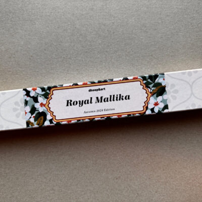 Räucherstäbchen-Verpackung 'Royal Mallika' von dhoop&art, Autumn 2024 Edition. Die längliche weiße Box zeigt ein elegantes Designelement in der Mitte - ein ornamentierter Rahmen mit dem Produktnamen, umgeben von weißen Jasminblüten mit grünen Blättern. Die Verpackung hat ein dezentes, helles Blumenmuster an beiden Enden.