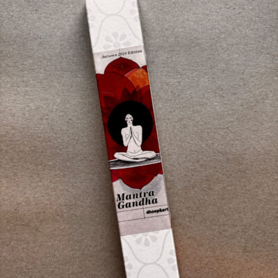 Räucherstäbchen-Verpackung 'Mantra Gandha' von dhoop&art, Autumn 2024 Edition. Die längliche weiße Box zeigt eine minimalistische Illustration einer meditierenden Figur in Lotusposition vor einem dunklen Kreis, umgeben von stilisierten roten und orangefarbenen Lotusblüten. Die Verpackung hat ein dezentes, helles Blumenmuster an beiden Enden.