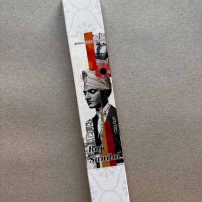 Räucherstäbchen-Verpackung 'Raj Sandal' von dhoop&art, Autumn 2024 Edition. Die längliche weiße Box zeigt ein modernes Schwarz-Weiß-Design mit einem Porträt im Turban, architektonischen Elementen und roten Akzenten. Die Komposition ist im Collage-Stil gehalten mit einer roten Blüte und geometrischen Elementen. Die Verpackung hat ein dezentes, helles Blumenmuster an beiden Enden.