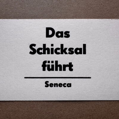 Letterpress Postkarte mit kurzem Seneca-Zitat in schwarzer Super Groteske auf weißem Büttenpapier: 'Das Schicksal führt'. Dreizeilig mit horizontalem Trennstrich und Signatur darunter, zentriert im traditionellen Handsatz gedruckt.