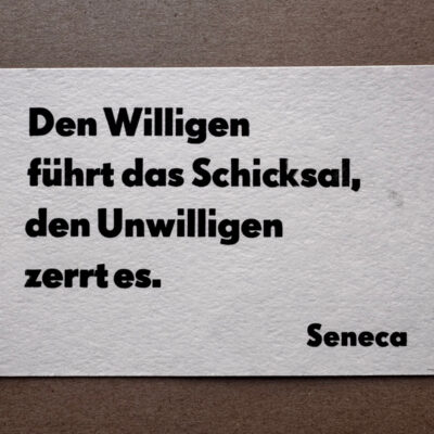 Letterpress Postkarte mit Seneca-Zitat in schwarzer Super Groteske auf weißem Büttenpapier: 'Den Willigen führt das Schicksal, den Unwilligen zerrt es.' Vierzeilig gesetzt mit rechtsbündiger Signatur, im traditionellen Handsatz gedruckt.