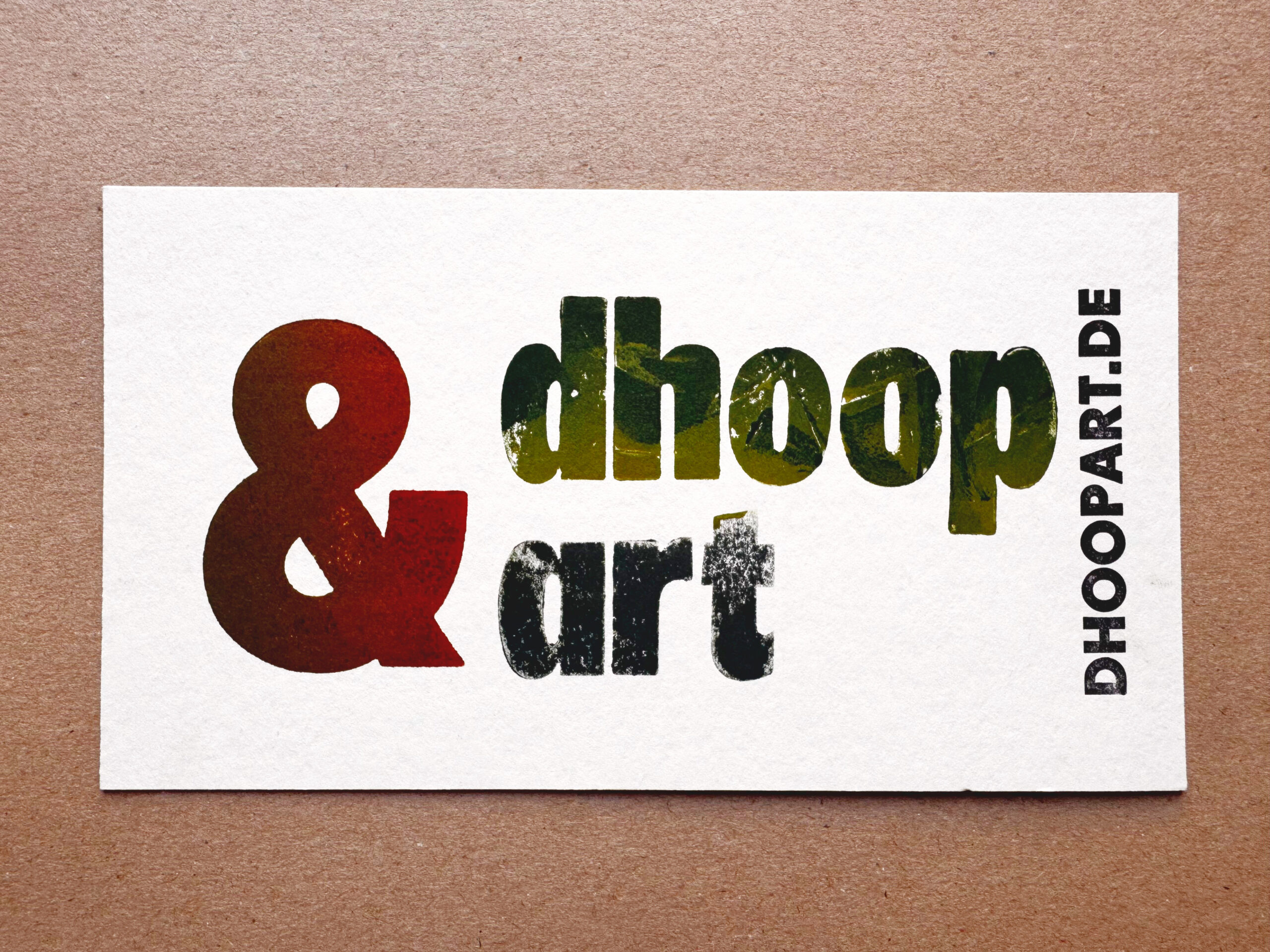 Visitenkarte im Letterpress-Druck. Logo 'dhoop&art' mit orangefarbenem Kaufmanns-Und, grünem 'dhoop' und blauem 'art'. Domain 'DHOOPART.DE' vertikal in schwarzer Super Groteske. Auf weißem Büttenpapier handgedruckt.